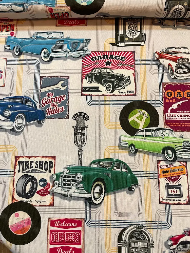 Farbenfroher Dekostoff als Meterware im Vintage-Stil mit klassischen Oldtimern, Jukeboxen, Schallplatten und amerikanischen Werkstatt-Schildern.