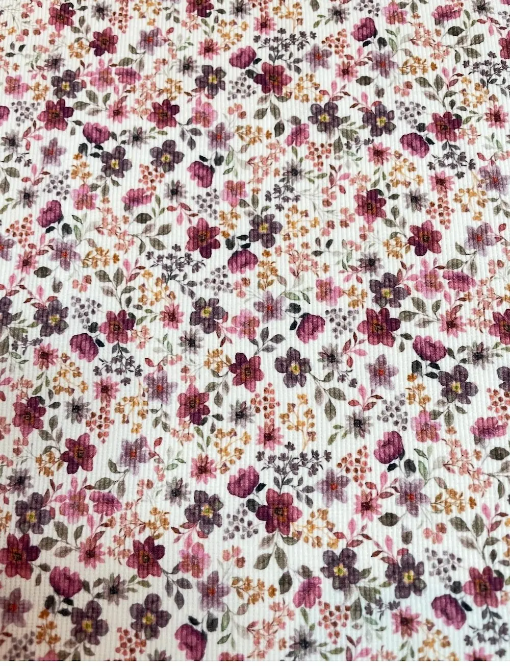 Weicher Rippjersey Stoff als Meterware mit romantischem Streublumen-Muster in Beere, Altrosa und Ocker auf hellem Grund.