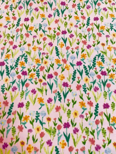 Rosa Jersey-Stoff mit dichtem Muster aus bunt illustrierten Wildblumen und Kräutern in Lila, Orange und Gelb.