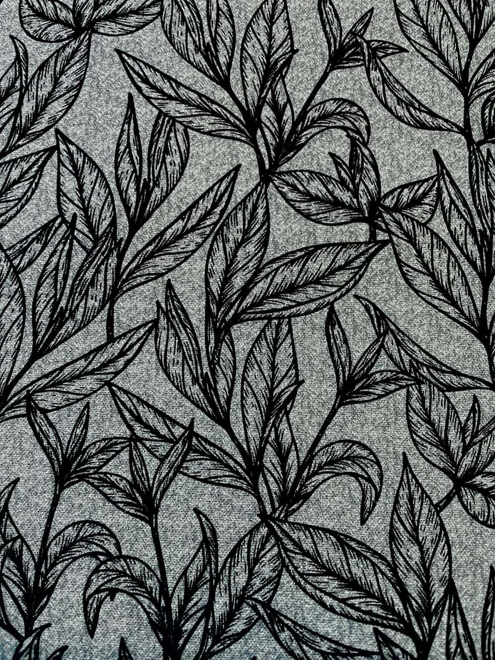 Strukturierter Canvas Dekostoff als Meterware in Meliert-Grau mit einem eleganten, schwarzen Linienmuster aus botanischen Blättern und Zweigen.
