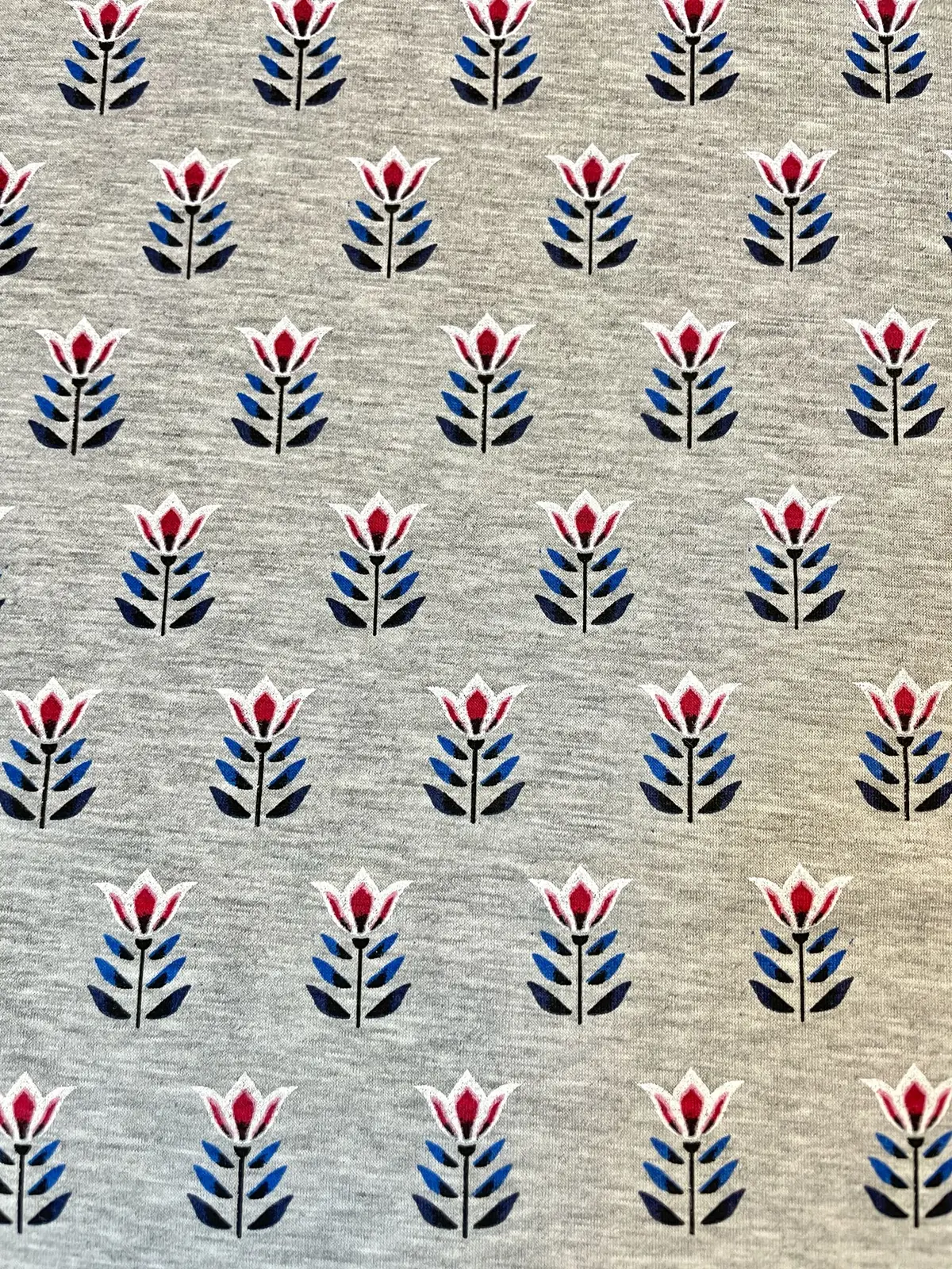 Hochwertiger Baumwolljersey als Meterware in Grau-Meliert, bedruckt mit einem regelmäßigen, geometrischen Retro-Muster aus rot-weißen Tulpen und dunkelblauen Blättern. Ideal für Bekleidung wie Shirts, Kleider und Kinderkleidung.