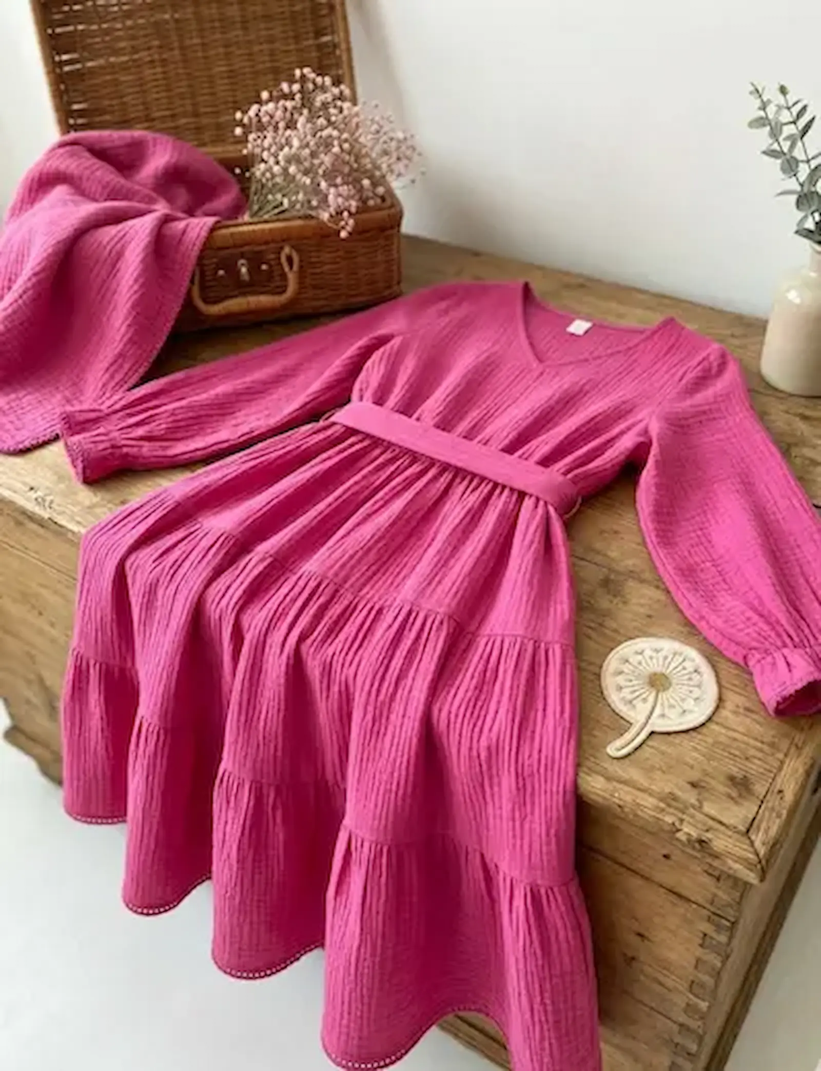 Langärmeliges Stufenkleid aus pinkem Musselin Stoff auf einer Holzkiste, farbenfrohe Double Gauze Baumwoll-Meterware für Damen- und Kinderkleidung.