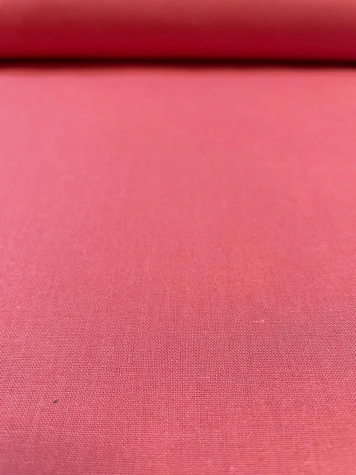 Fein gewebter Uni-Baumwollstoff in Coral beziehungsweise Lachsrosa als Meterware aus nächster Nähe.