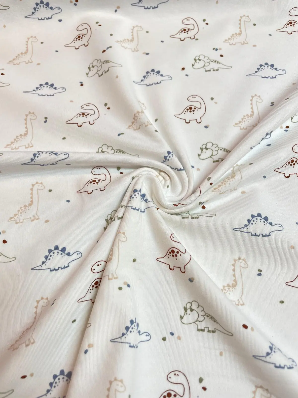 Gezwirbelter weißer Jersey-Stoff mit einem Muster aus verschiedenen Dinosauriern in gedeckten Blau-, Grün- und Brauntönen.