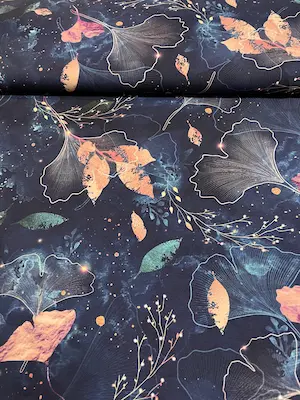 Dunkelblauer Jersey-Stoff mit einem künstlerischen Print aus filigranen Ginkgo-Blättern und abstrakten Blättern. Das Design besticht durch aquarellartige Farbverläufe in Kupfer, Rosa und Smaragdgrün sowie feine Lichteffekte auf einem tiefblauen Hintergrun