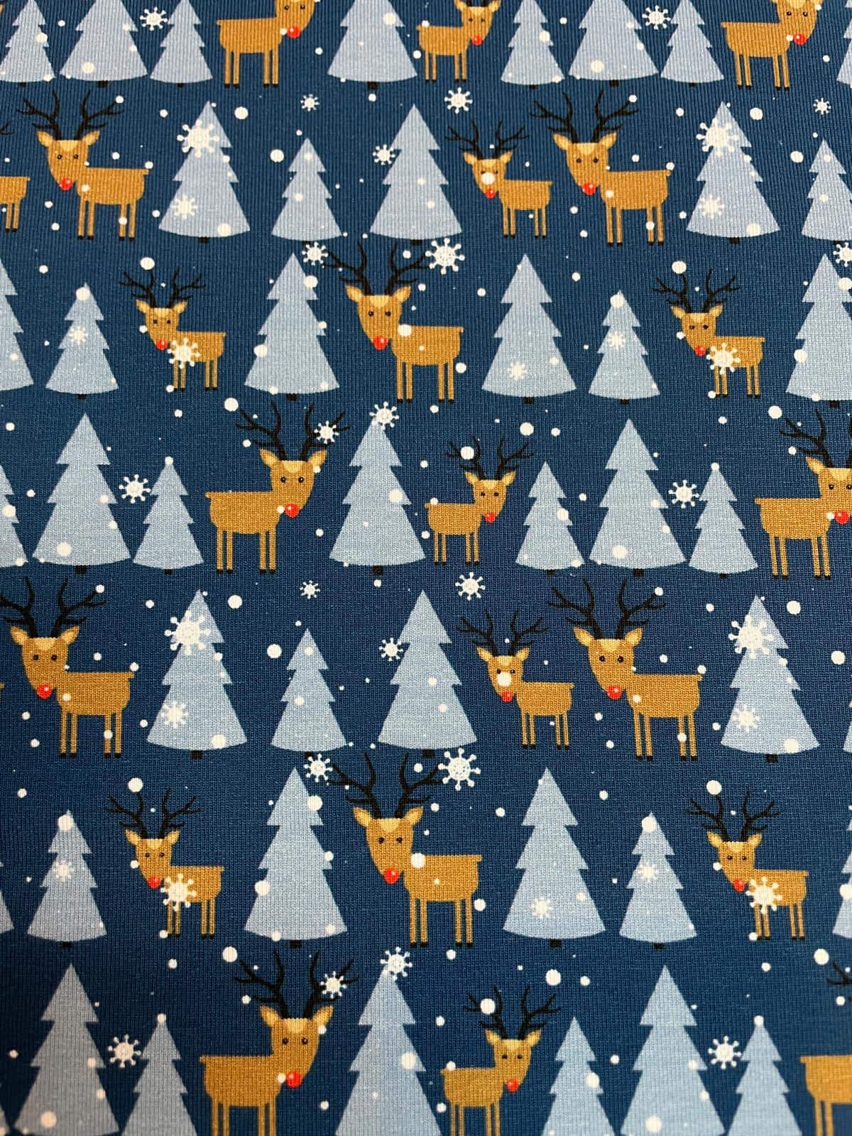 Blauer Jersey-Stoff als Meterware mit weihnachtlichem Rentiermotiv, hellblauen Tannenbäumen und fallenden Schneeflocken