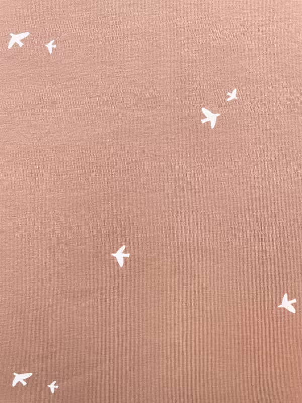Elastischer Baumwolljersey in der Farbe Terracotta mit einem Muster aus kleinen, weißen Vögeln.